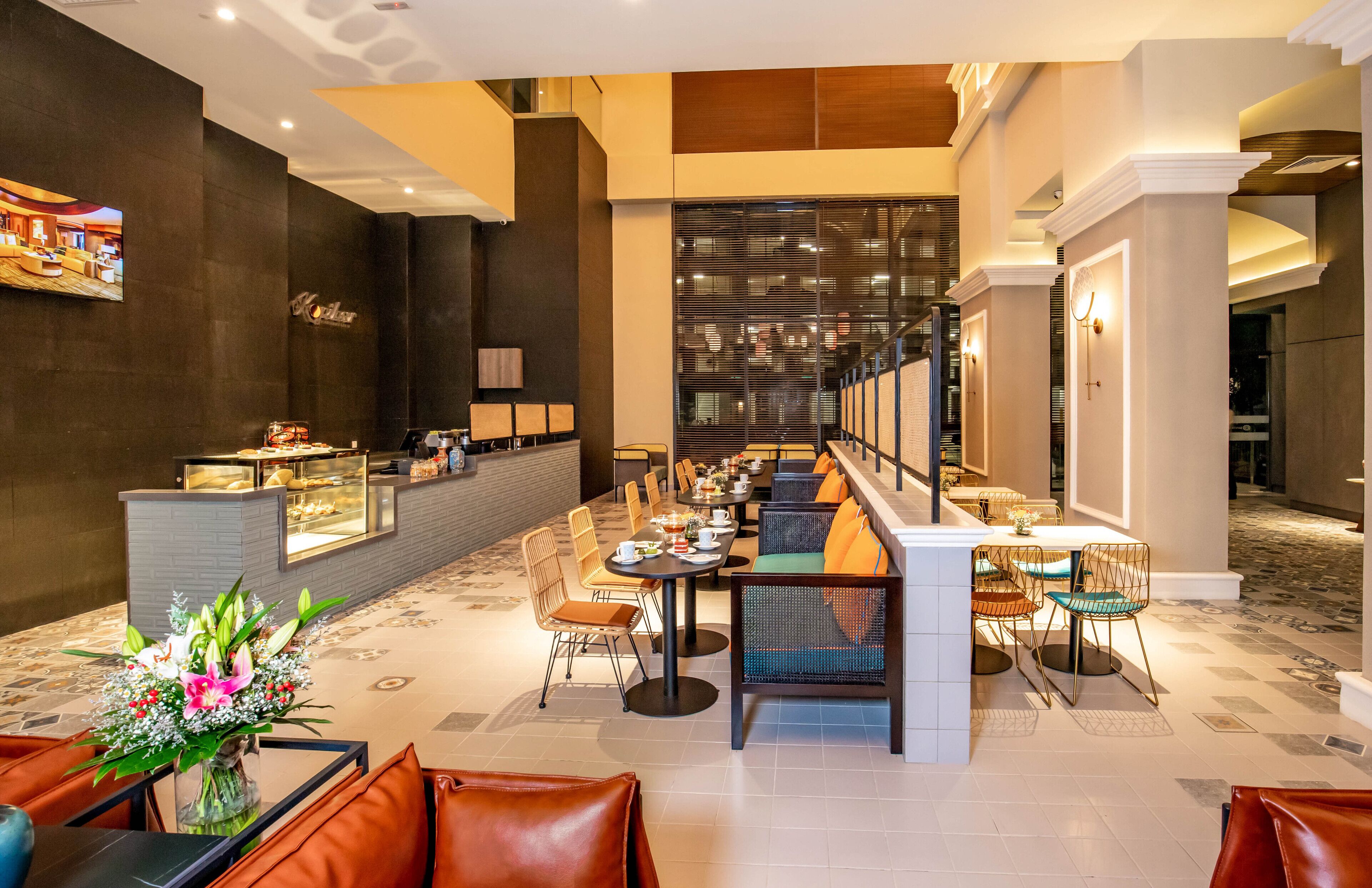 A modern hotel lobby with a long reception desk, multiple seating areas, and a decorative wall with a framed picture.