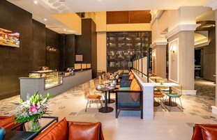 A modern hotel lobby with a long reception desk, multiple seating areas, and a decorative wall with a framed picture.