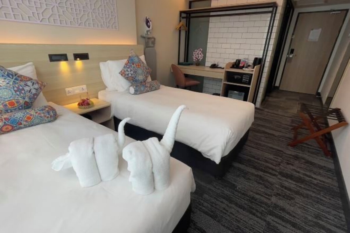 A hotel room with two beds, a desk, and a mirror. There are towels on the beds and a chair in the corner.