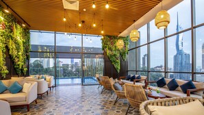 A modern lounge with a view of the city skyline, featuring hexagonal patterned flooring, wicker furniture, and green vertical gardens. - Santa Grand Signature Kuala Lumpur (Kuala Lumpur)