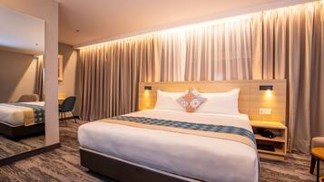 A hotel room with a large bed, a desk, a chair, a bedside table, and a mirror.