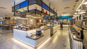 A modern hotel kitchen with a buffet setup, including a central island with a pot and plates, and a variety of food items displayed on shelves and counters. - Santa Grand Signature Kuala Lumpur (Kuala Lumpur)