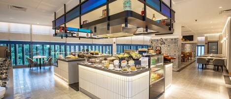A modern hotel lobby with a central buffet area, seating arrangements, and large windows offering a view of the outdoors.