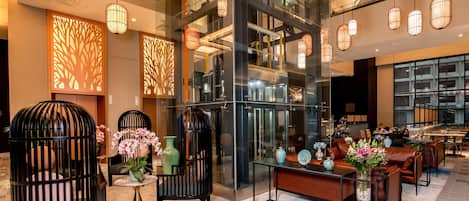 A modern lobby with glass partitions, black cushioned seating, and hanging pendant lights.