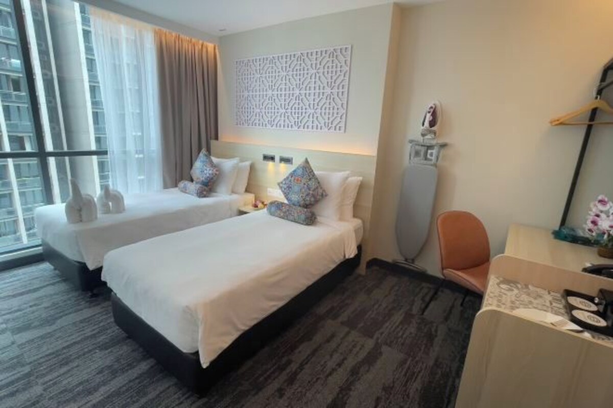 A hotel room with two beds, a desk, a chair, a decorative wall panel, and a window with curtains.