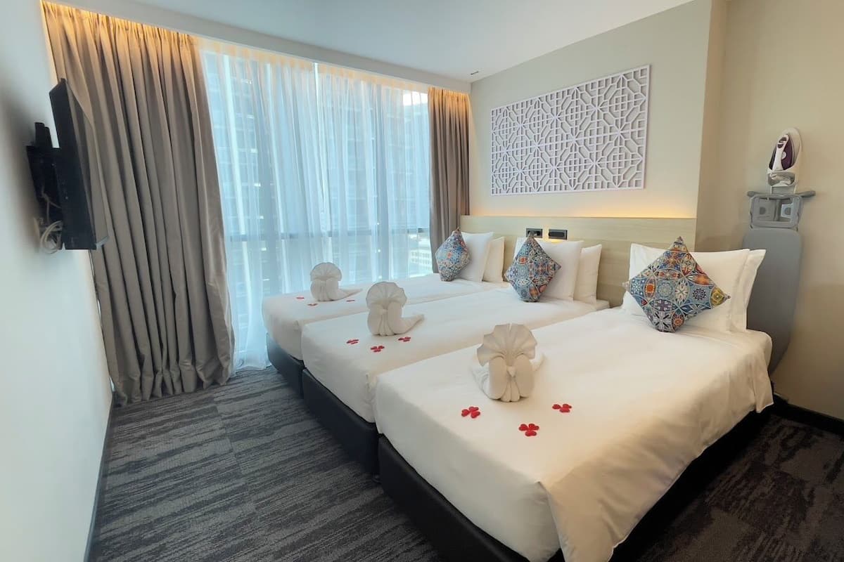A hotel room with three beds, a TV mounted on the wall, a decorative wall panel, and a shoe rack.