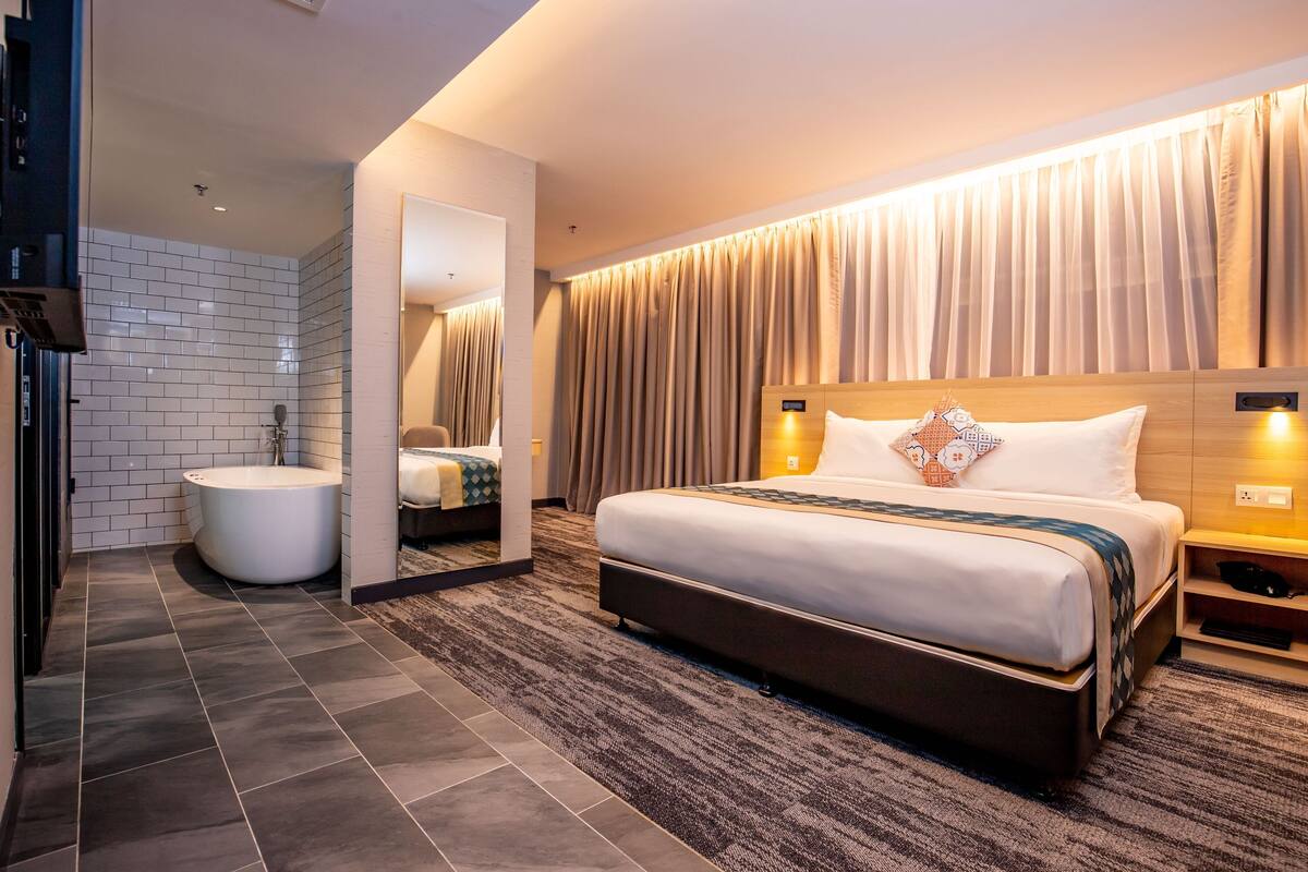 A modern hotel room with a large bed, a separate bathroom, and a mirror reflecting the room.