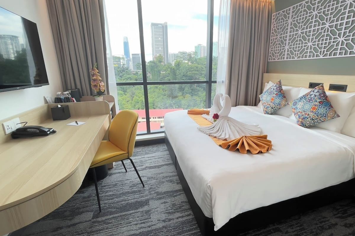 A hotel room with a bed, a desk, a chair, a TV, and a view of the city.