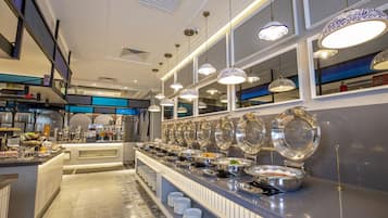 A buffet setup with multiple serving stations, a variety of food items, and overhead decorative lighting.