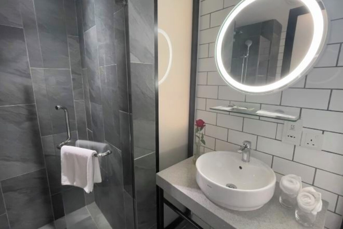 A modern bathroom with a glass-enclosed shower, a white sink with a round mirror, and a rose decoration.