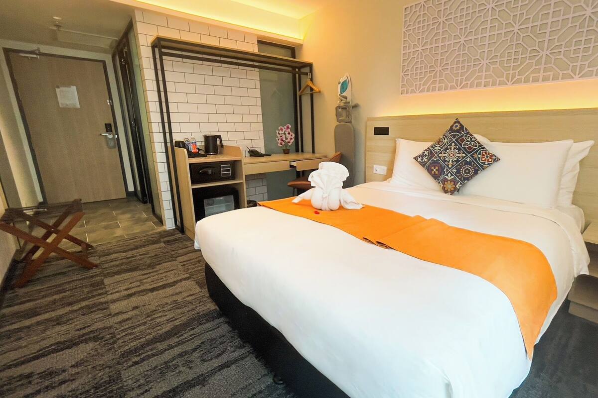 A hotel room with a bed, a desk, a mirror, and a bathroom.