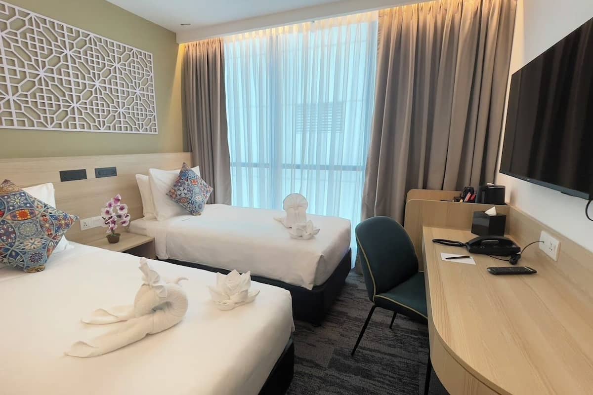 A hotel room with two beds, a desk, a chair, a TV, and a decorative wall panel.