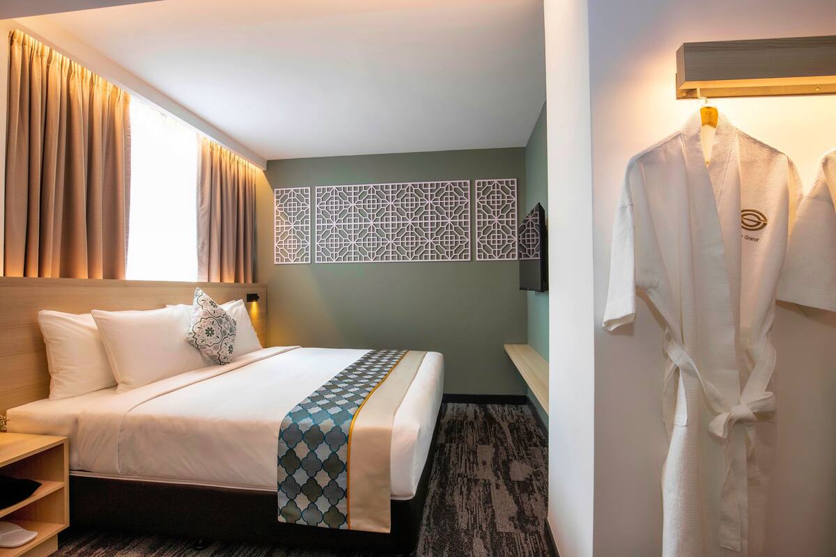 A hotel room with a bed, a robe hanging on the wall, and a patterned wall decoration.