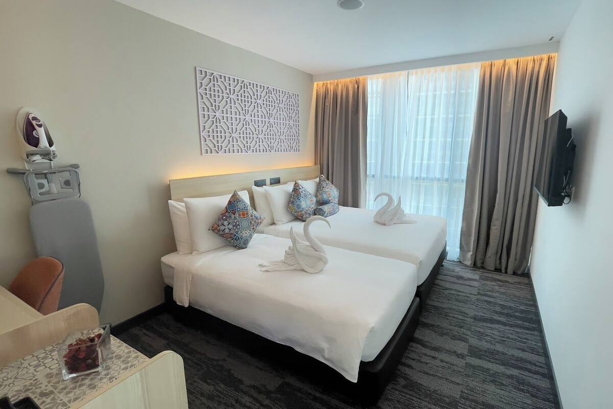 A hotel room with two beds, a TV, a decorative wall piece, and a window with curtains.