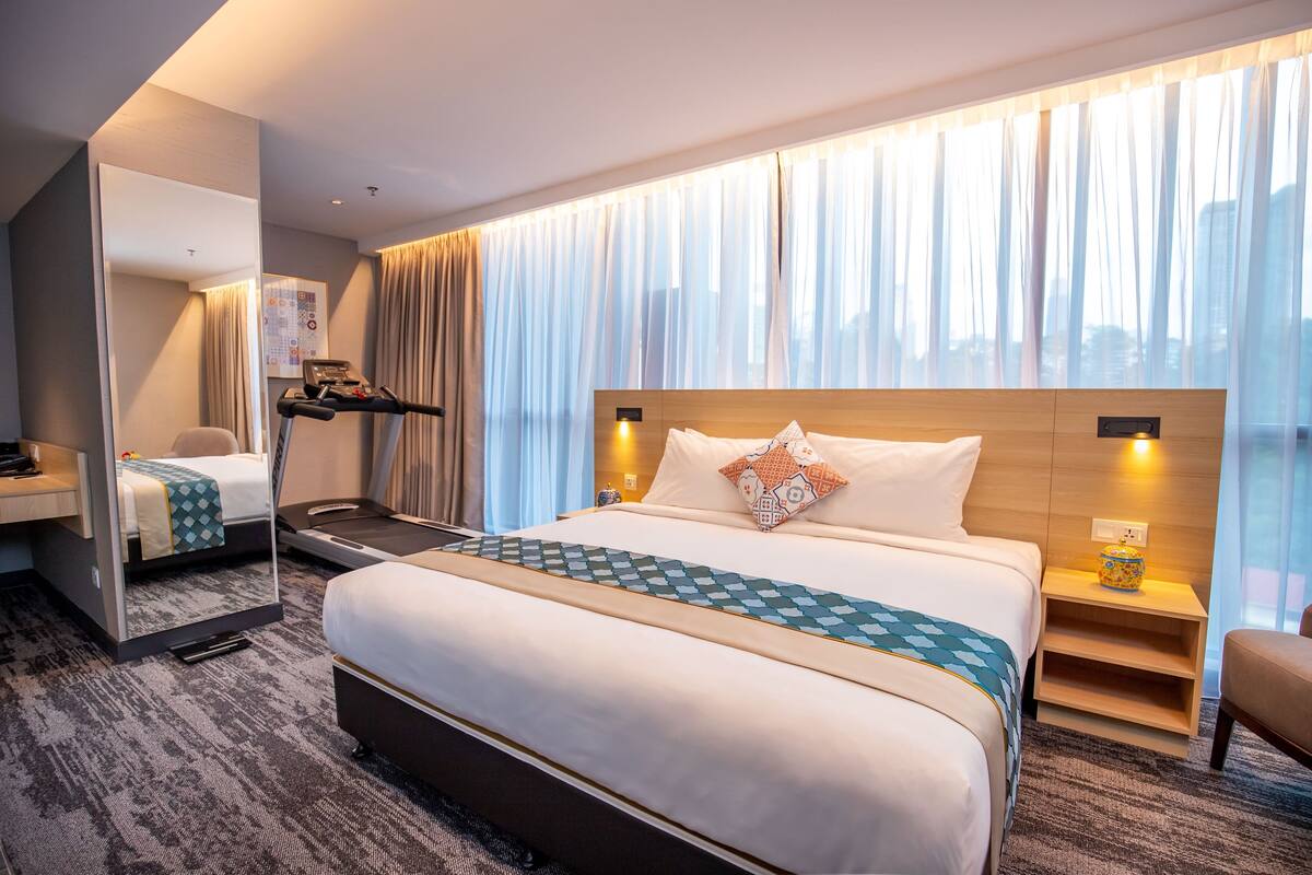 A hotel room with a large bed, a desk, a chair, a mirror, and a window with curtains.
