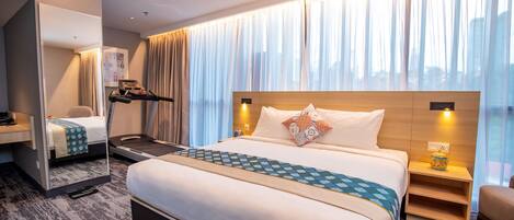 A hotel room with a large bed, a desk, a chair, a mirror, and a window with curtains.