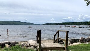 Un muelle de madera que se adentra en un lago, con barcos al fondo y un paisaje montañoso.