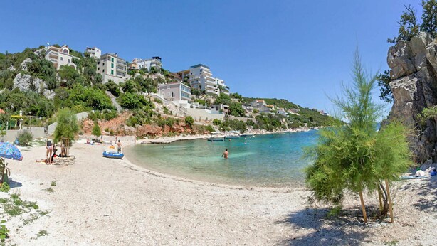 A beach with clear waters, a few boats, and buildings on a hillside.