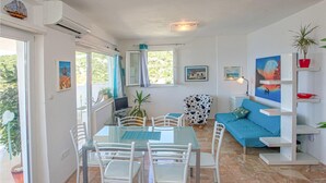 A modern living room with a dining area, featuring a blue sofa, white chairs, and a glass table.