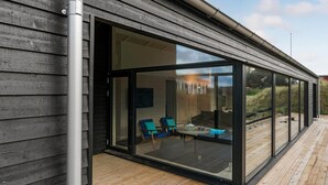 Et moderne hus med en stor glasdør, der fører til et udendørs opholdsområde med blå stole.