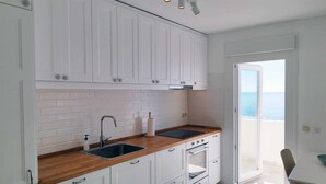 A modern kitchen with white cabinets, a wooden countertop, a sink, and an oven. There is a sliding glass door leading to a balcony with a view of the sea. - 1 bedroom , city centre, front line beachsea views (Estepona)