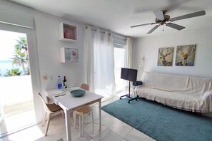 Une pièce comprenant une table à manger, des chaises, un canapé, un ventilateur de plafond, des œuvres d’art accrochées au mur et une vue sur l’océan par une fenêtre.
