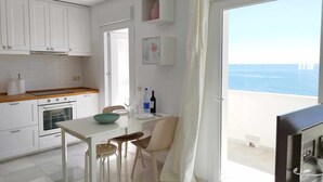 A kitchen with white cabinets, a wooden countertop, and a dining area with a table and chairs. A large window offers a view of the sea. - 1 bedroom , city centre, front line beachsea views (Estepona)