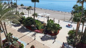 A beachside promenade with palm trees, a pool area, and a view of the ocean. - 1 bedroom , city centre, front line beachsea views (Estepona)