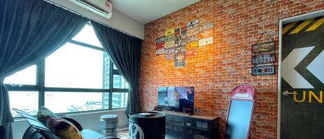 A room with a brick wall, a large window, a TV, and a 'Welcome' sign.