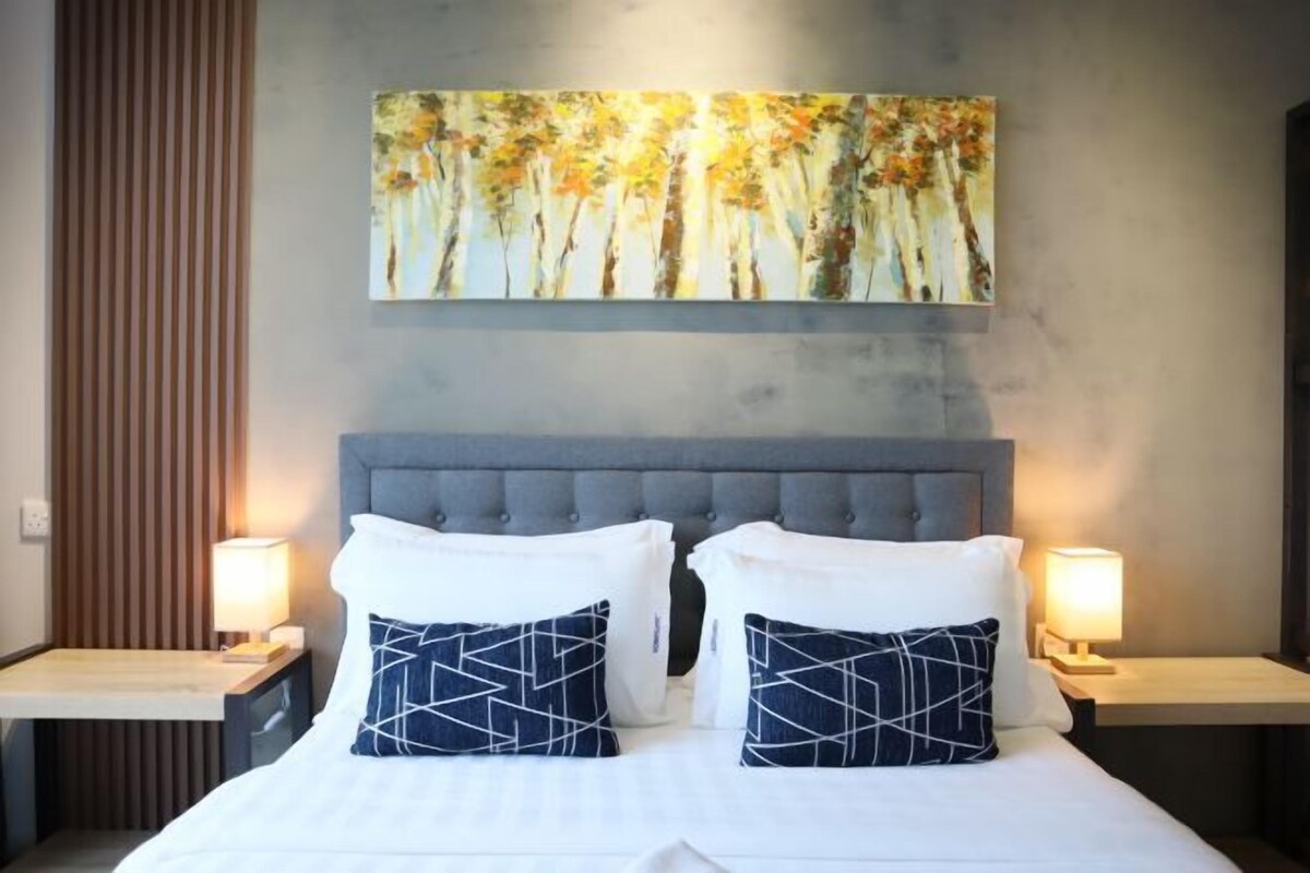 A hotel room with a large bed, two bedside tables, and a wall-mounted painting.