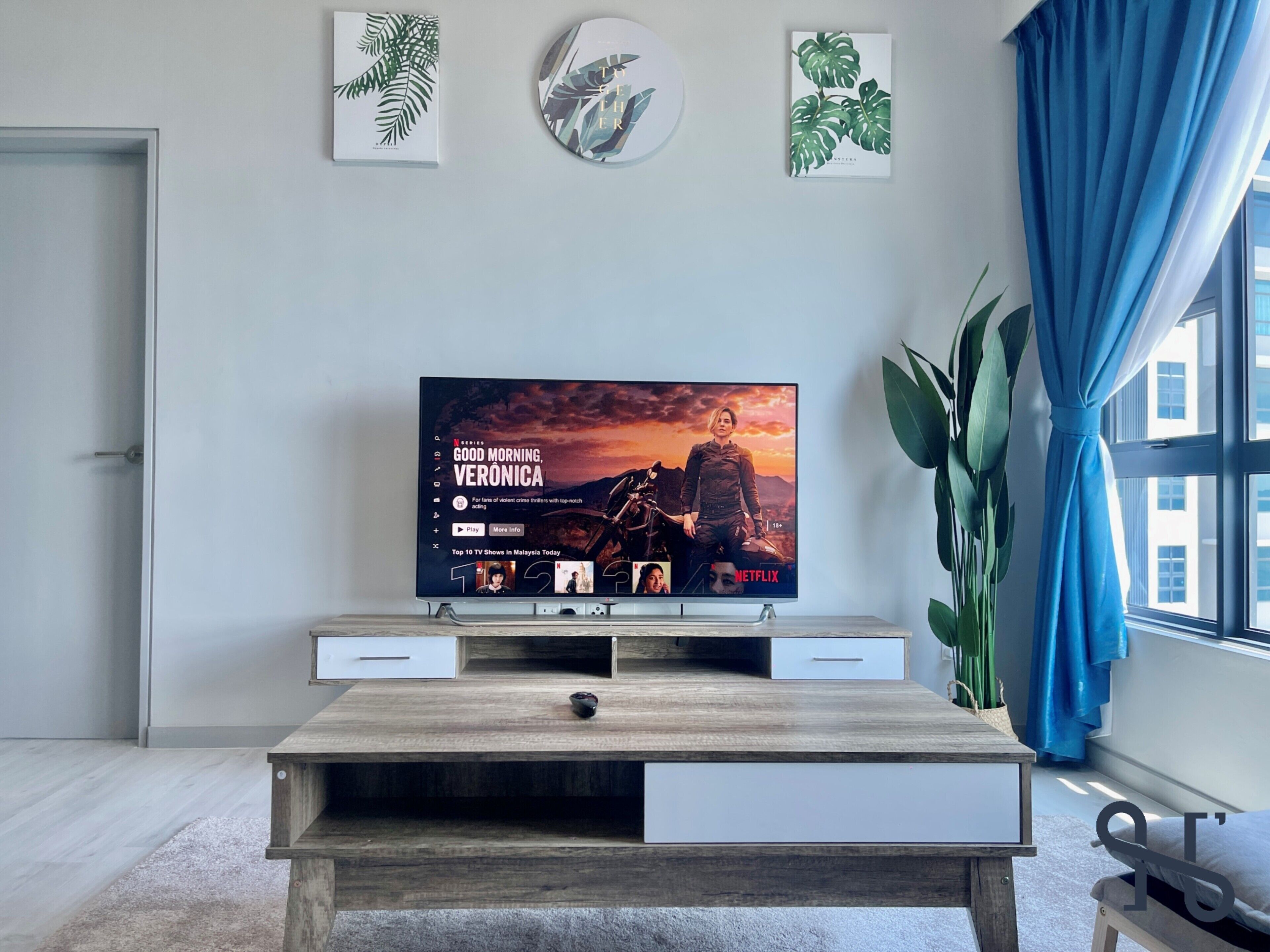 Una sala moderna con un televisor de pantalla plana, una mesa de centro de madera y un gran ventanal con cortinas azules.