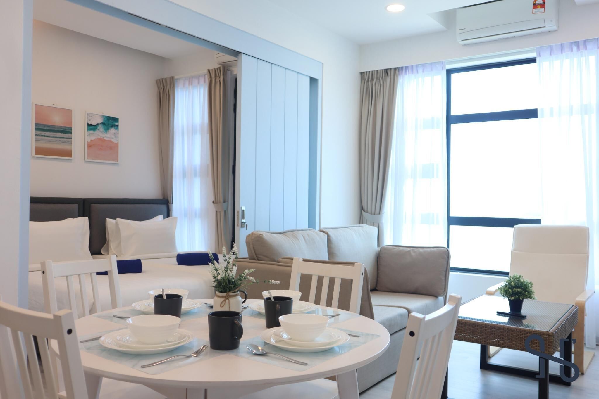 Una habitación de hotel moderna con una cama, un sofá, una mesa de comedor con platos y tazas, y un ventanal con cortinas.