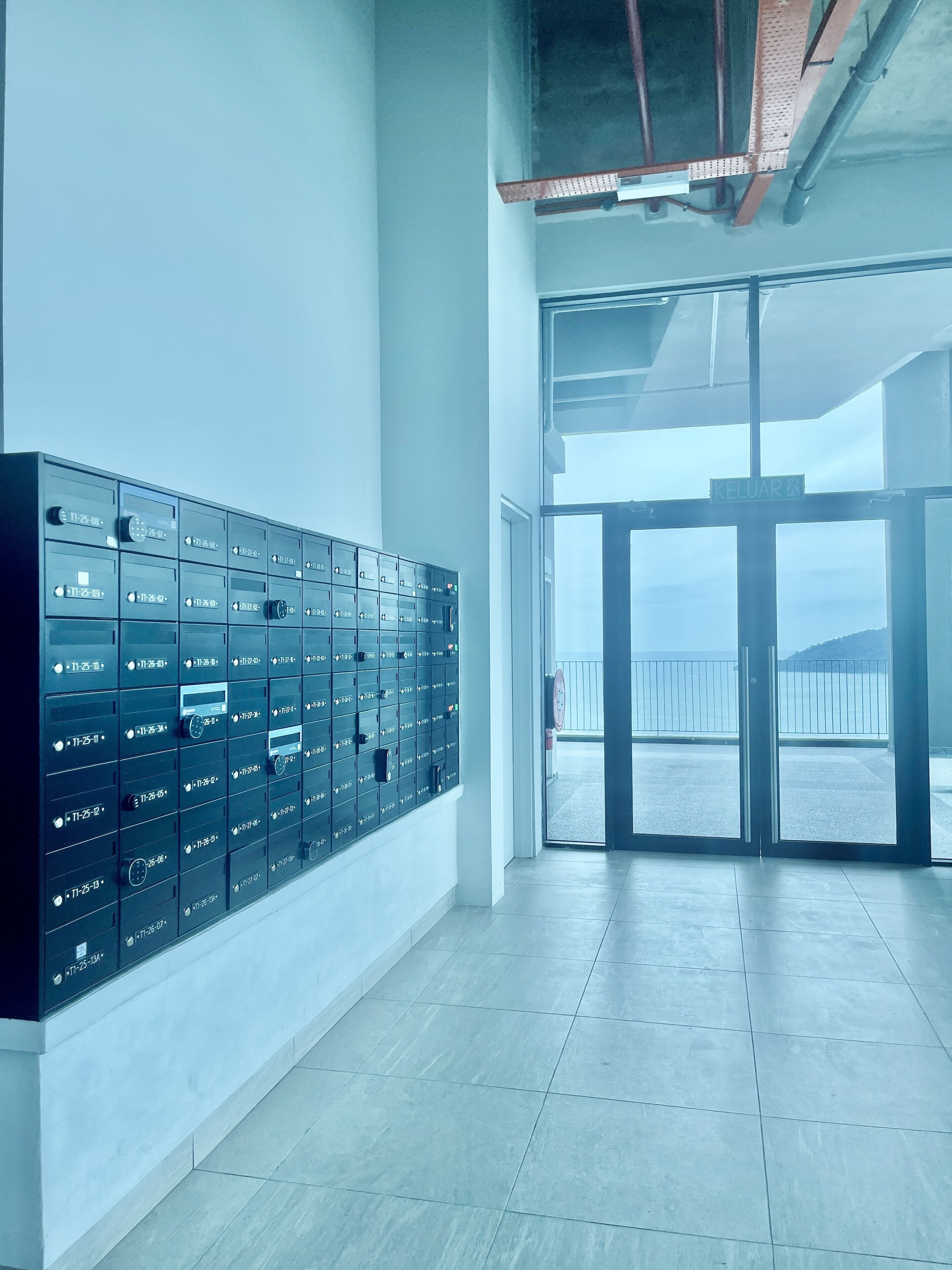 A modern hotel lobby with a row of black safes, a glass door leading to a balcony with a view, and a tiled floor.