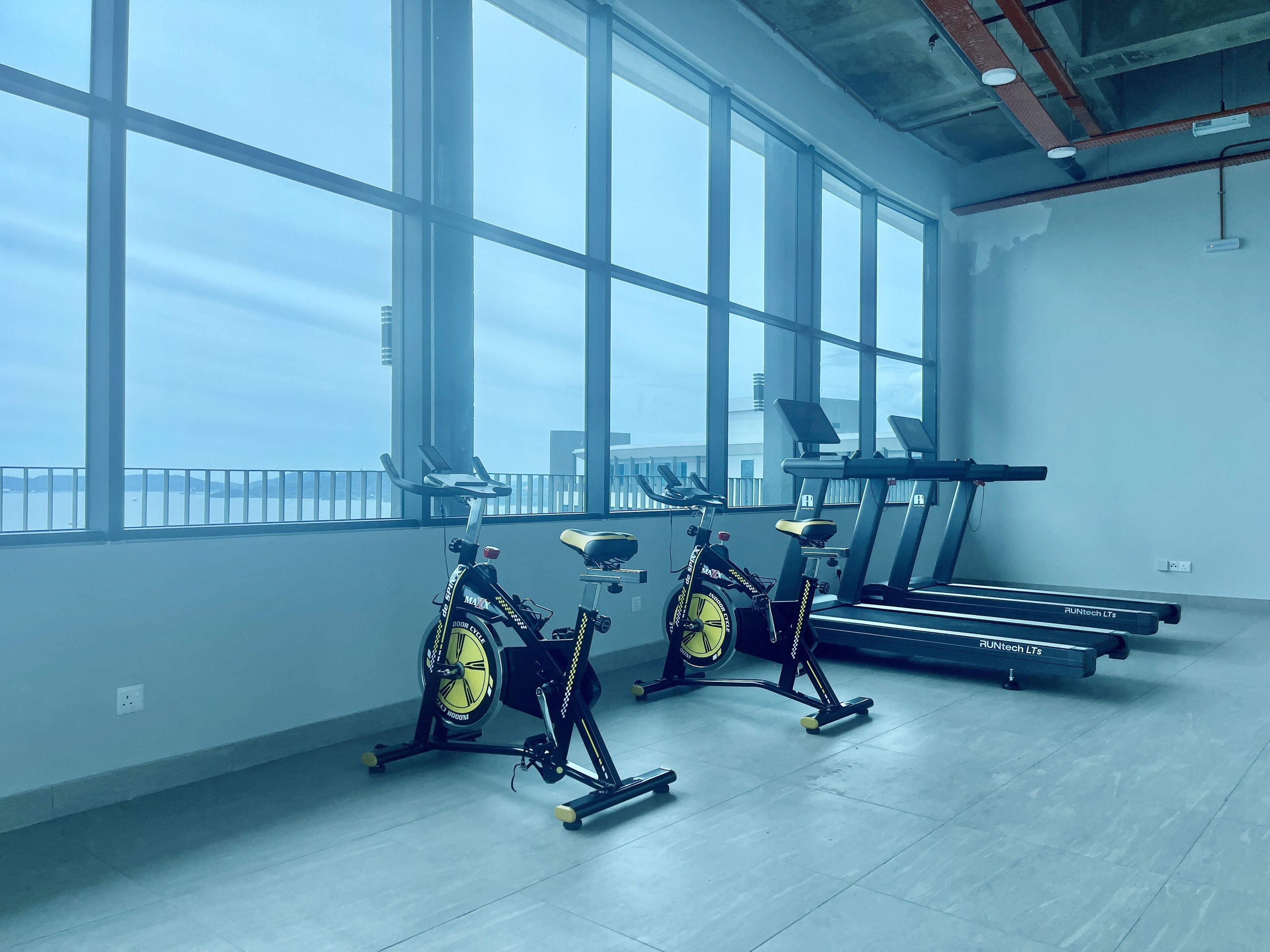 A gym with stationary bikes, treadmills, and large windows offering a view of the city.