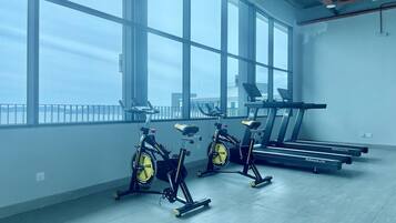 A gym with stationary bikes, treadmills, and large windows offering a view of the city.