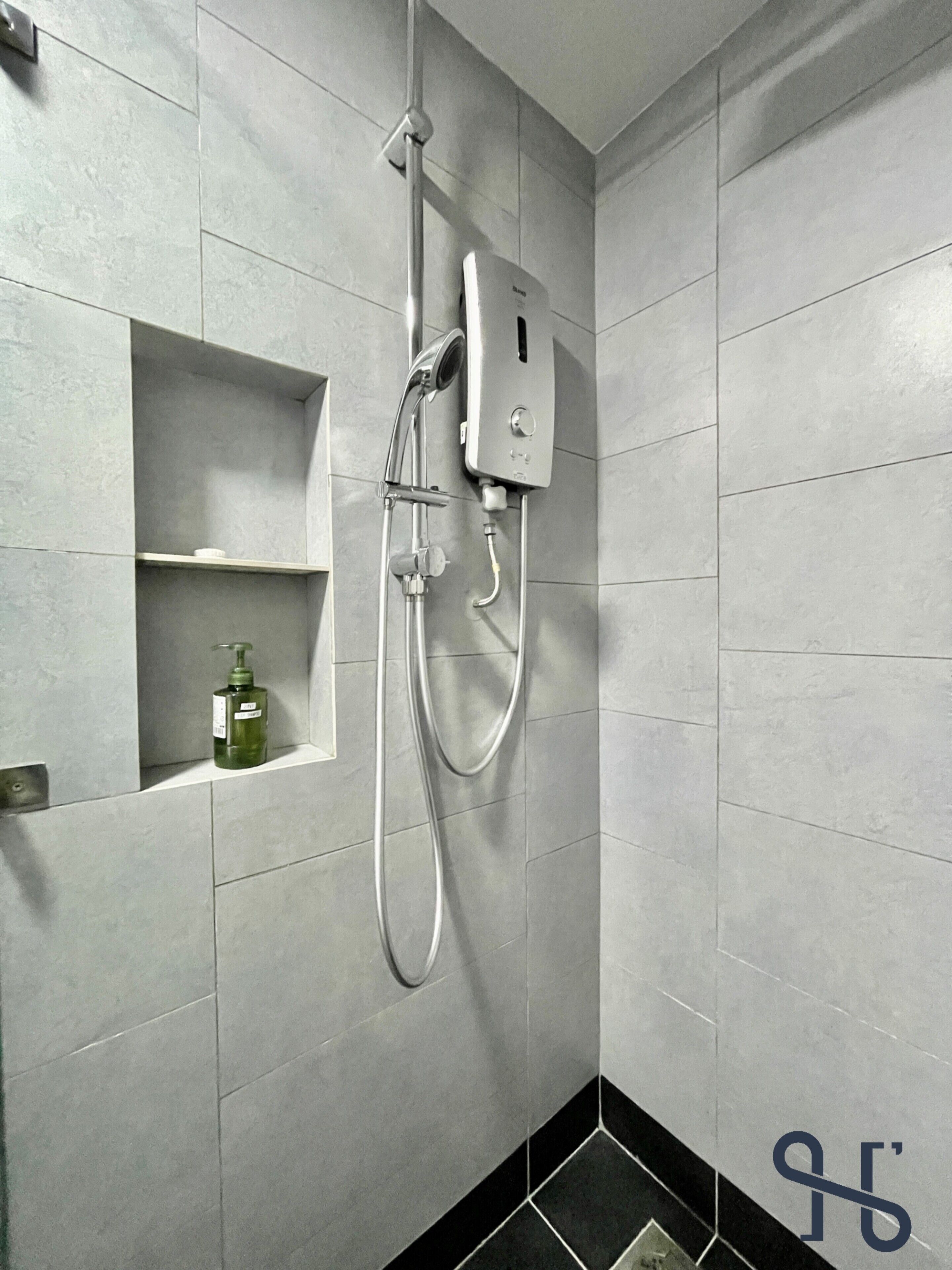 Une salle de bain avec des carreaux gris, une douche et une étagère sur laquelle se trouve une bouteille.
