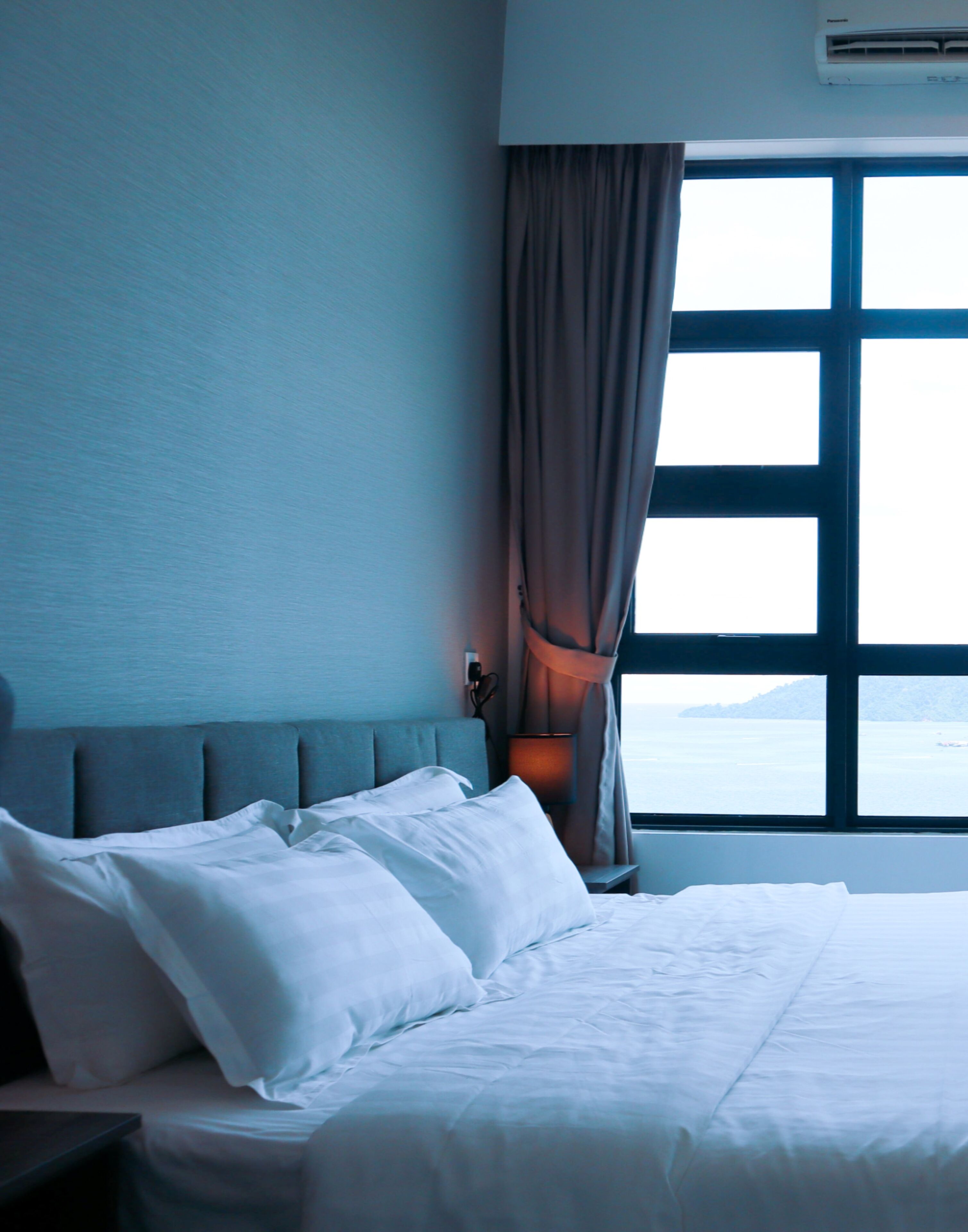 Una habitación de hotel con una cama, una mesita de noche, una lámpara y una ventana con cortinas.
