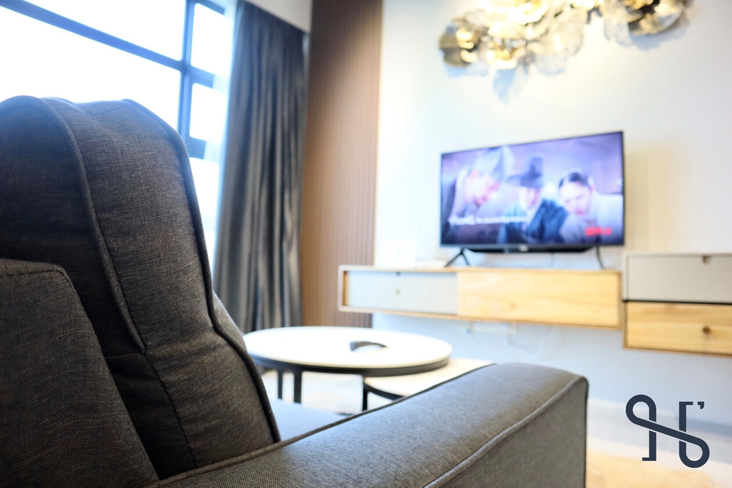 A modern living room with a grey sofa, a television on the wall, and a small round table.