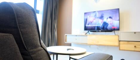 A modern living room with a grey sofa, a television on the wall, and a small round table.