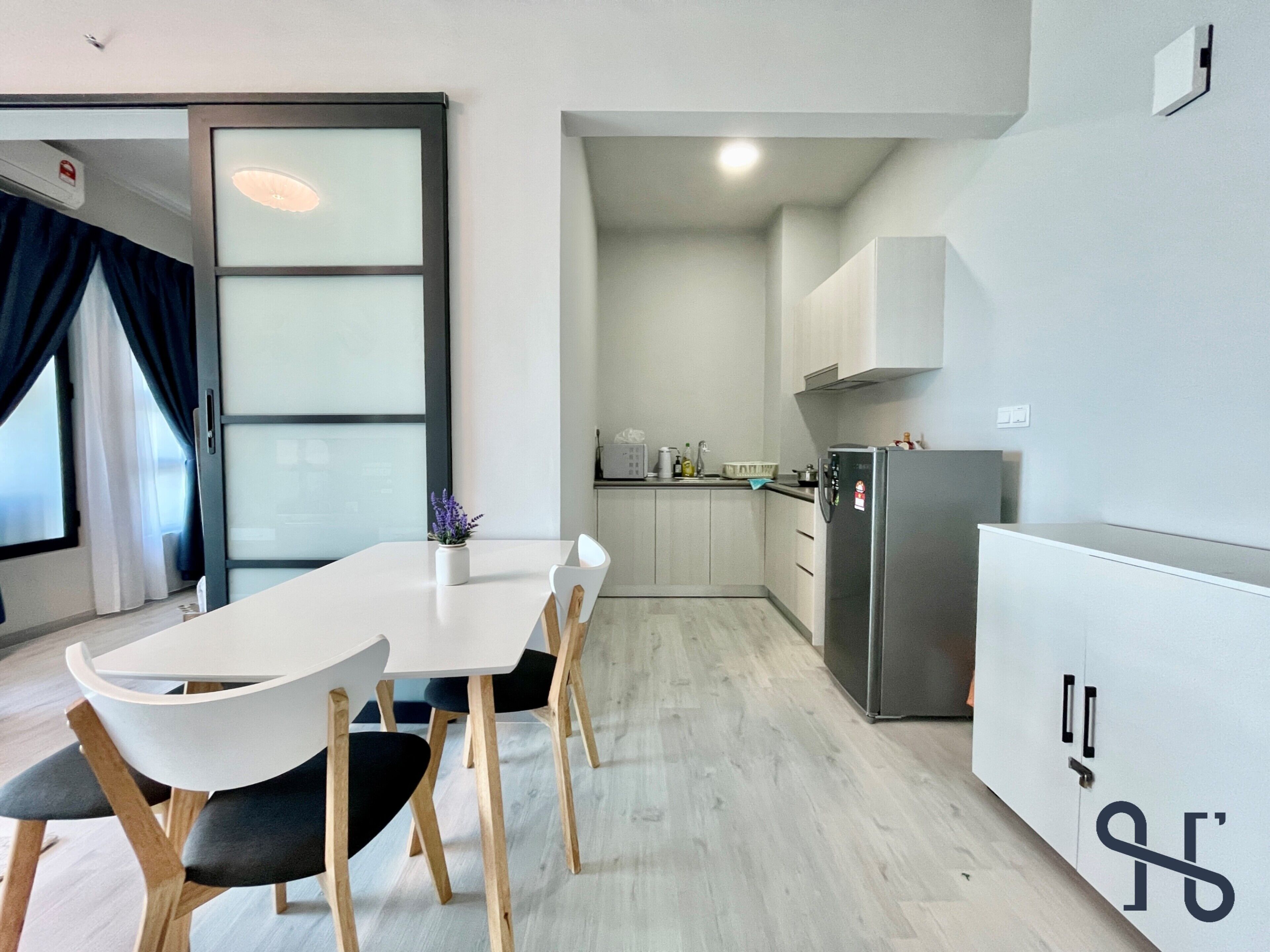 Cozinha moderna com armários brancos, geladeira de aço inoxidável e área de jantar com mesa e cadeiras brancas.