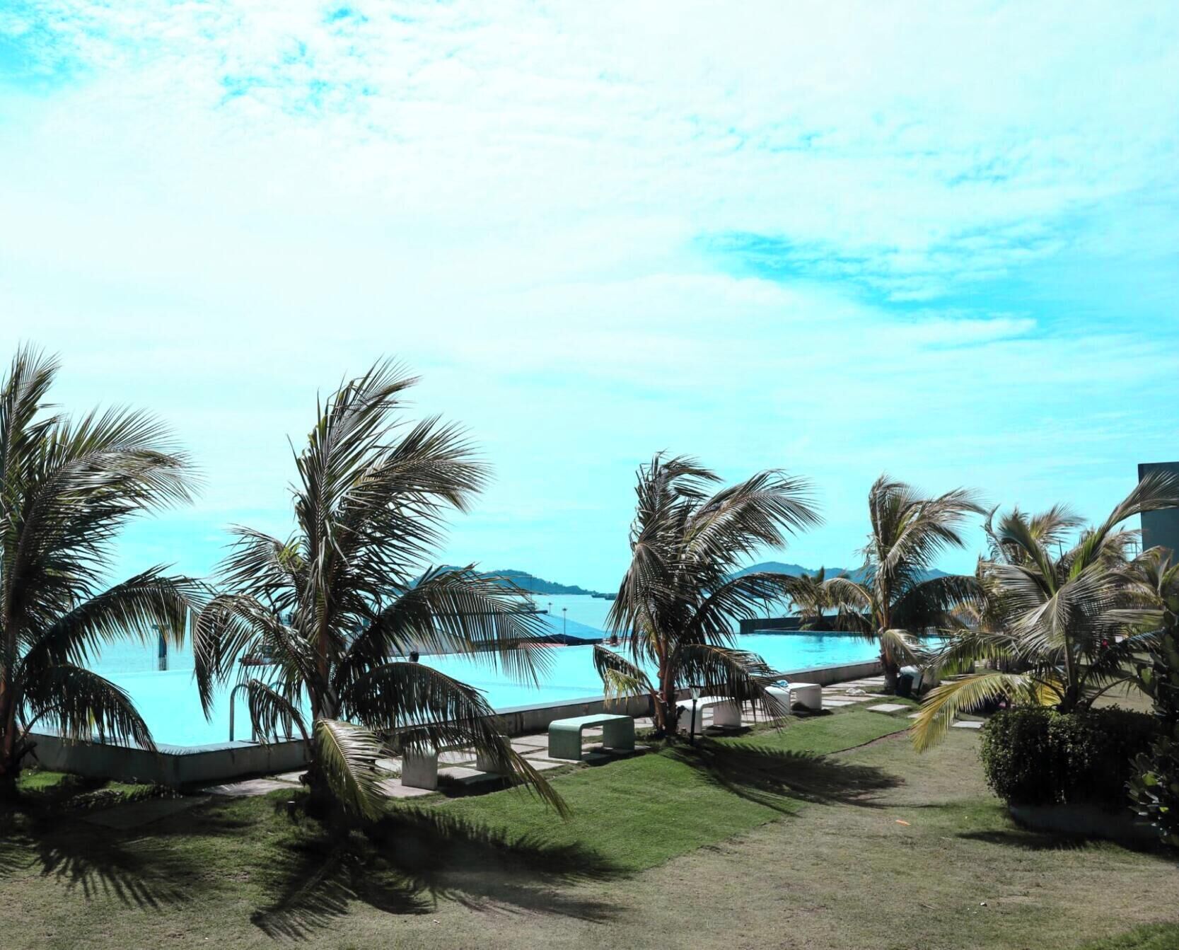 A resort with a pool, palm trees, and a view of the sea.