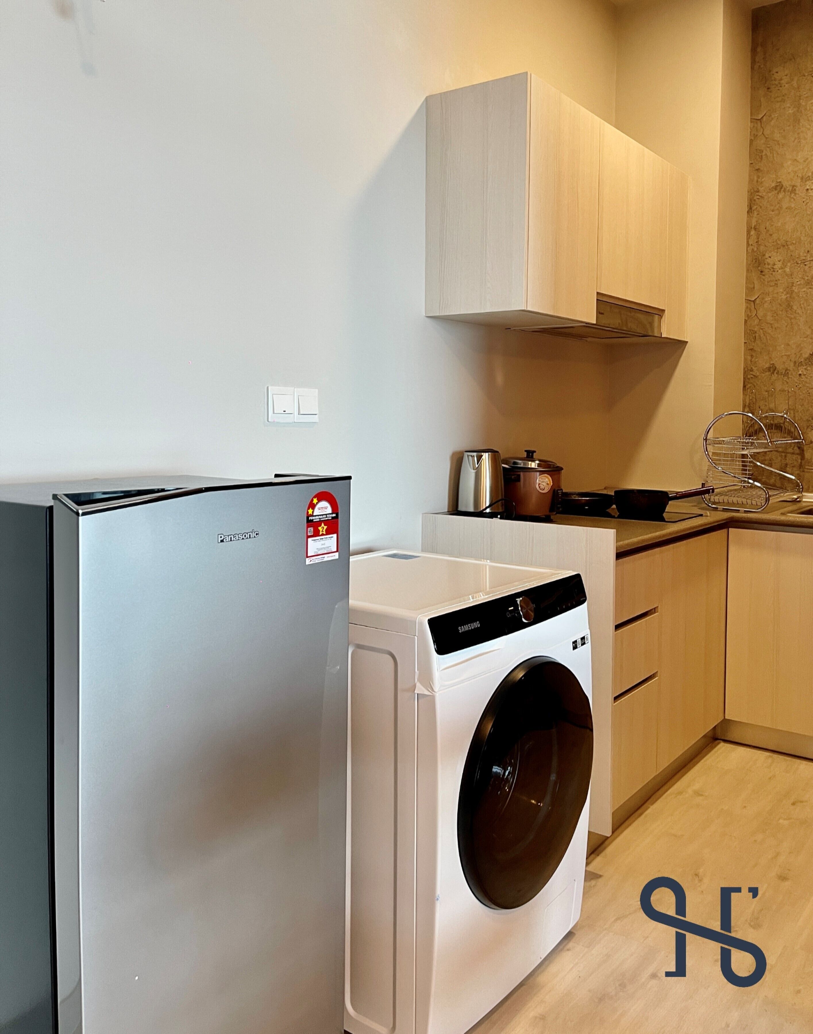 A compact kitchen with a washing machine, a refrigerator, and wooden cabinets.
