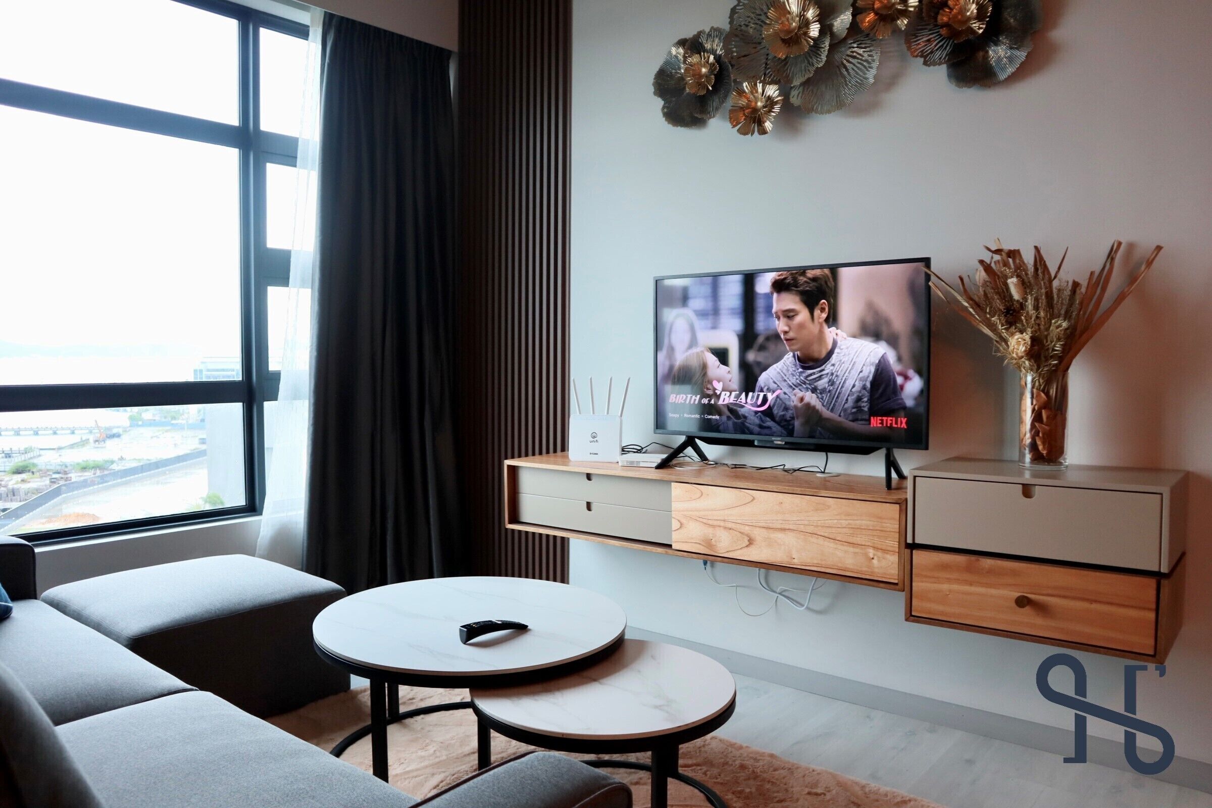Egy modern nappali, melyben található egy síkképernyős televízió, egy kanapé, egy dohányasztal és egy díszes váza.