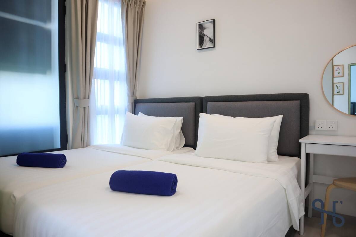 Une chambre d’hôtel avec un lit double, deux oreillers, une serviette bleue, une table de chevet et un miroir.