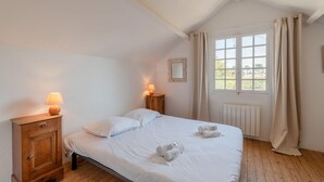 A bedroom with a bed, bedside tables, a lamp, a window with curtains, and a view outside. - La Paisible - 50m mer - Jardin (La Bernerie-en-Retz)