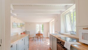 A kitchen with a tiled floor, wooden cabinets, a dining table with chairs, and a window providing natural light. - La Paisible - 50m mer - Jardin (La Bernerie-en-Retz)