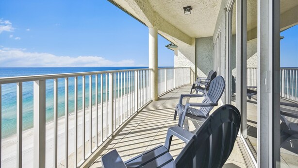 A balcony with a view of the ocean, featuring a railing and a few chairs.
