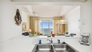 A modern kitchen with a large window, a two-basin sink, and a dining area with wicker furniture.