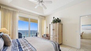 A bedroom with a bed, a ceiling fan, a wardrobe, and a view of the ocean.