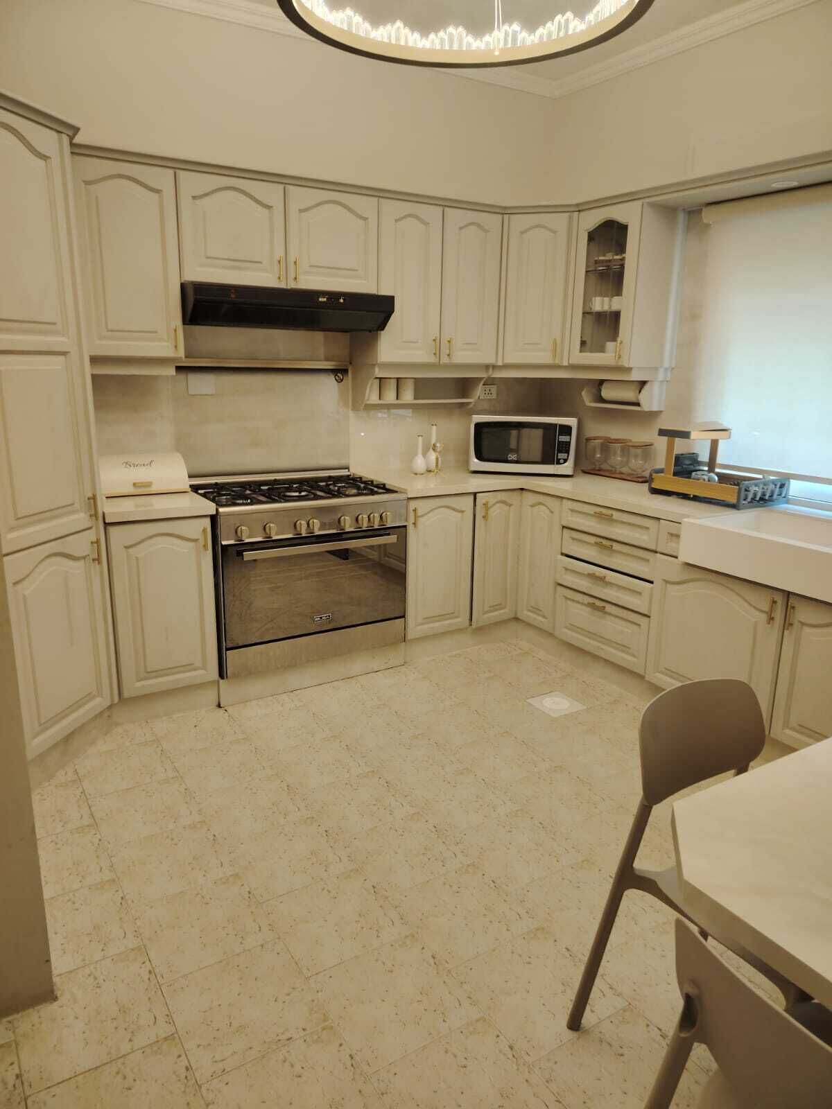 A compact kitchen with white cabinetry, a gas stove, an oven, a microwave, and a small dining area with a chair.